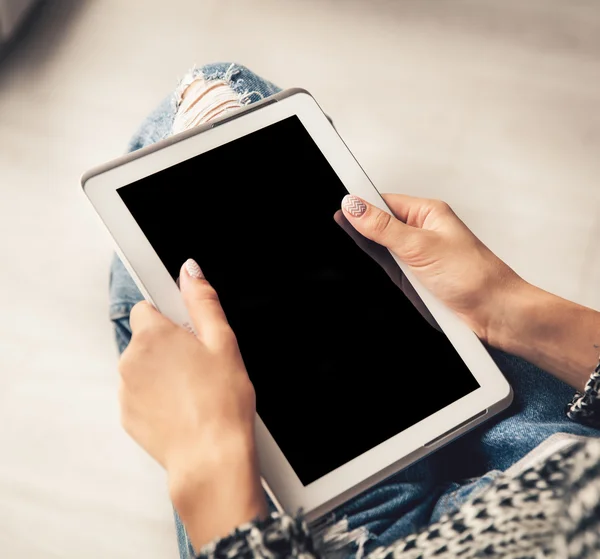 Woman holding and using tablet with empty screen, ripped jeans