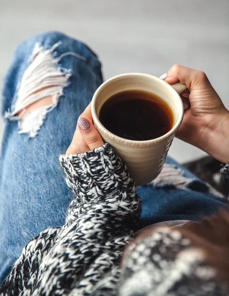 Girl's hands holding a cup of coffee, ripped jeans