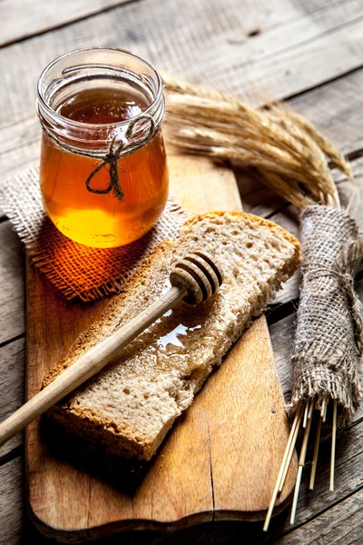Honey in a jar, slice of bread, wheat on an old vintage planked wood table.