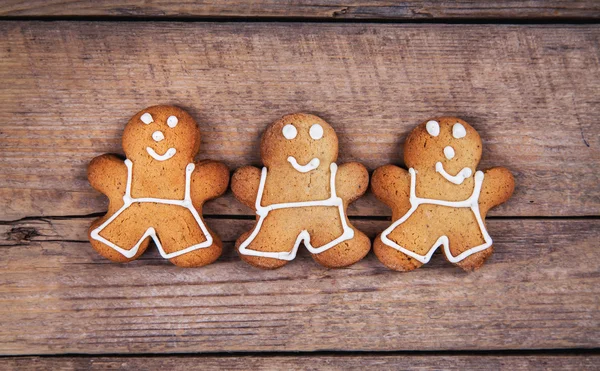 HIgh angle view of three gingerbread men on a rustic white kitchen table. The cookies are  plain and without icing.
