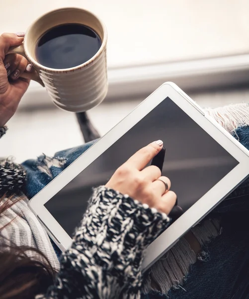 Soft photo of woman In the armchair with tablet and cup of coffee in hands, ripped jeans