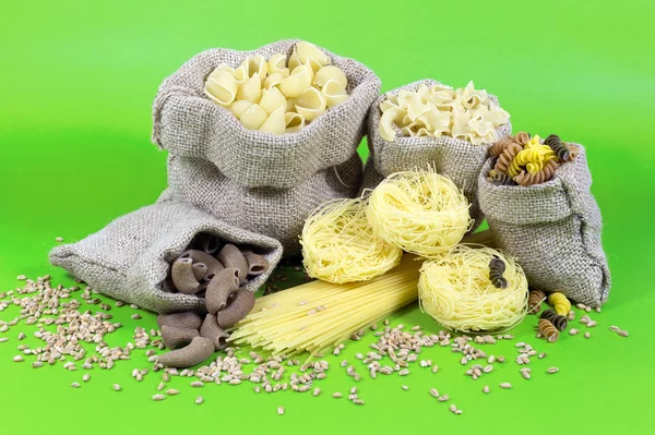 Jute Bags Filled with Pasta of Different Colors and Shapes Over Green Background