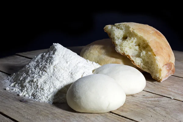 Stages of Making Bread-Flour, Dough and Loaf of Bread on Wooden Table Over Black Background