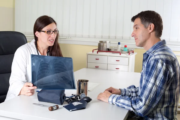 Doctor Explaining Lung X-ray Results to Middle Aged Patient in Consulting Room