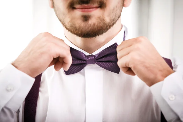 Man puts on violet bow tie.