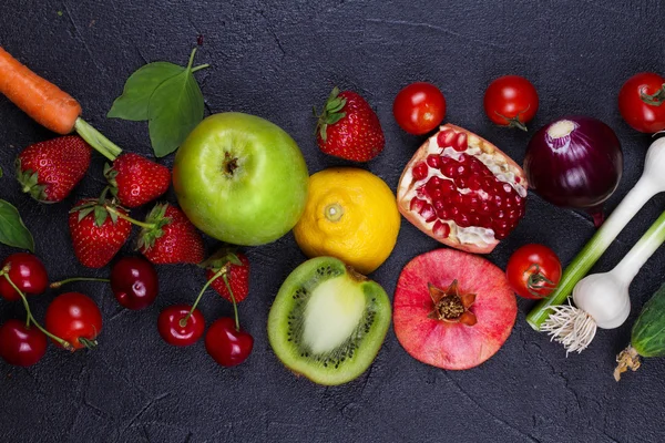 Carrot, beetroot, cucumber, lemon, pomegranate, kiwi, apples, tomatoes, cherries, strawberry, red onion, basil and mint. View from above, top studio shot of vegetables and fruits