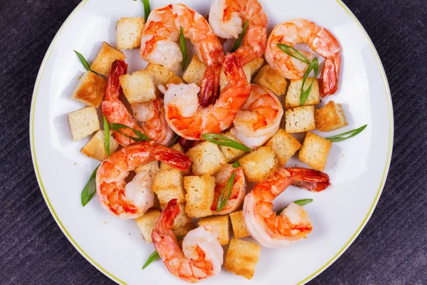Shrimp with crispy croutons and scallions in white plate. White wine bottle