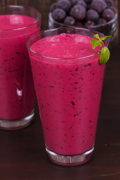Frozen summer berries smoothie garnished with mint on dark wooden background
