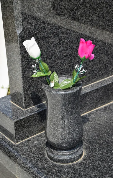 Flowers in a vase next to a tombstone in the cemetery