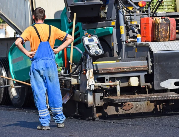 Construction worker next to an asphalt paving vehicle