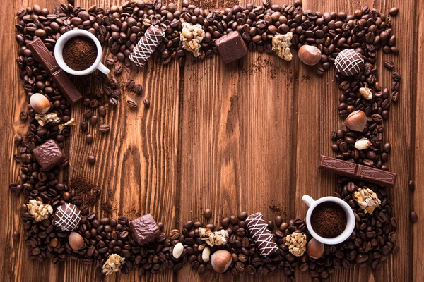 Roasted coffee beans, chocolate, candy, nuts, cup and the frame for inscriptions on wooden background