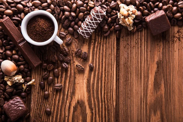 Roasted coffee beans, chocolate, candy, nuts, cup and the place for inscriptions on wooden background