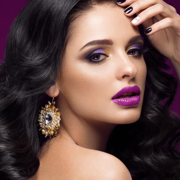 Beautiful brunette model: curls, classic makeup, gold jewelry and purple lips. The beauty face.