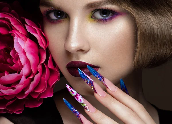 Beautiful girl with colorful make-up, flowers, retro hairstyle and long nails. Manicure design. The beauty of the face.