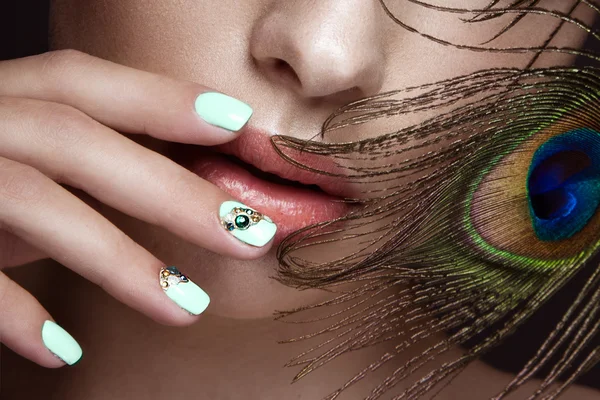 Beautiful girl with manicure design and peacock feather on her face. Art nails.