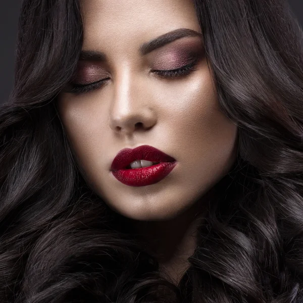 Beautiful brunette model: curls, classic makeup and red lips. The beauty face.
