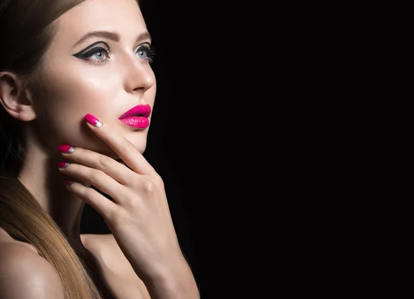 Beautiful girl with unusual black arrows on eyes and pink lips and nails. Beauty face. Picture taken in the studio on a black background.