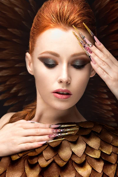 Beautiful girl in the image of the Phoenix with bright makeup, long fingernails and red hair. Beauty face.