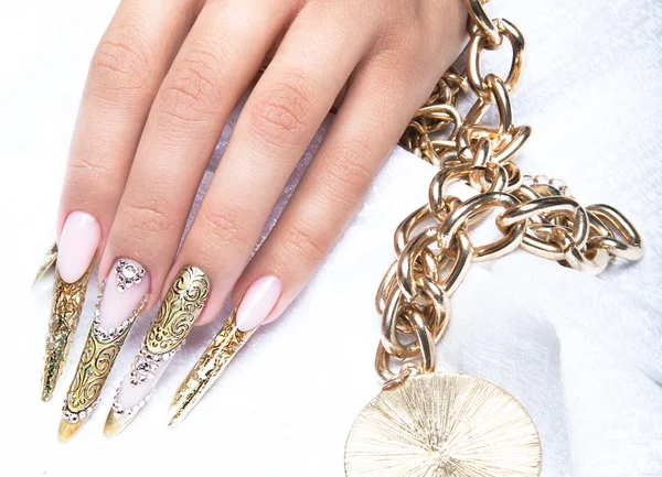 Beautiful long nails in a gold design with rhinestones. Nail art.