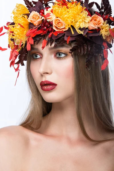 Beautiful  girl with bright autumn wreath of leaves and flowers. Beauty face. Picture taken in the studio on a white background.