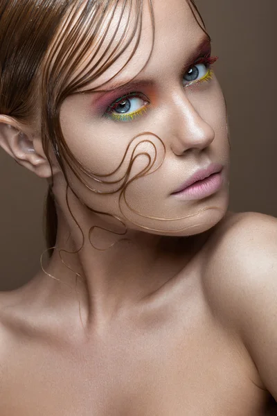 Beautiful girl with bright colored makeup and wet strands of hair on the face. Creative image.