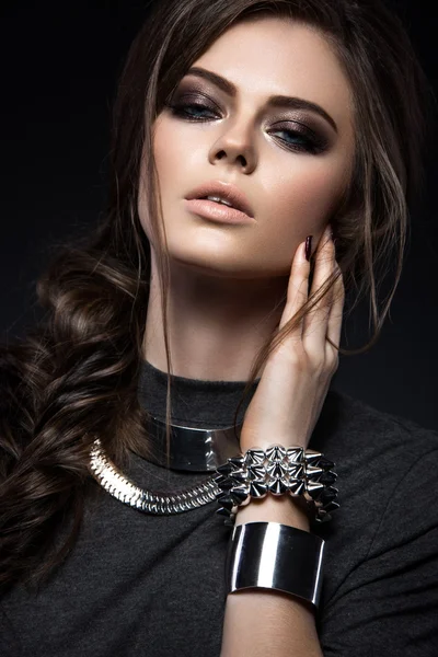 Beautiful girl with bright smokey make-up, perfect skin, black clothes, metal accessories and hairstyle as a braid.