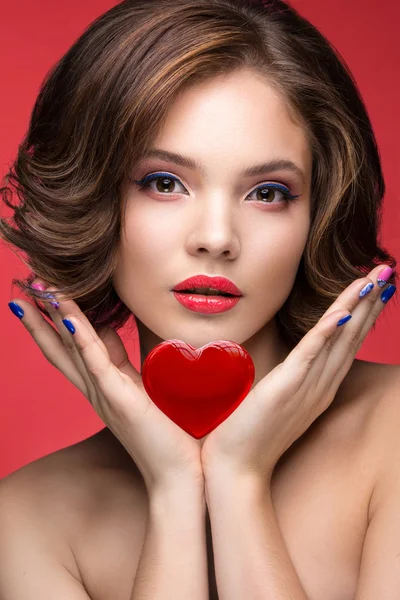 Beautiful model girl with bright makeup and red heart in the hands. Beauty face. Short colorful nails