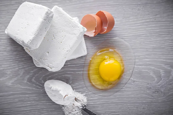 Cottage cheese, eggs and spoon flour on the wood background.