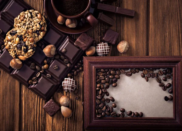 Roasted coffee beans, chocolate, candy, nuts, cup and the frame for inscriptions on the wooden background