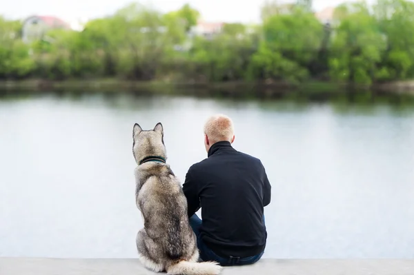 Dog and man sit on the river bank.