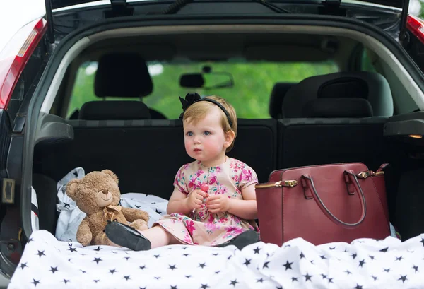 Little girl sits in luggage carrier of the family car.