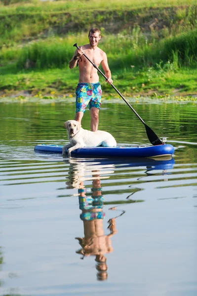 The dog and the man float by the boat on the lake.