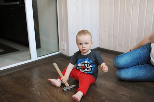 The kid sits on a floor in the room and plays with a hammer