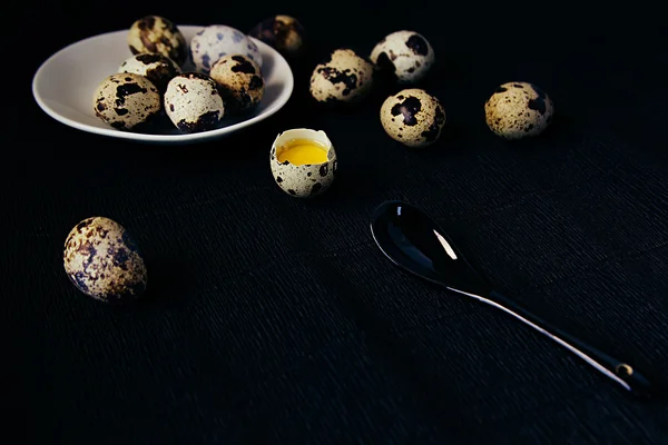 Quail eggs on a black textured background. Raw broken egg with the yolk. Easter card. Side view. Background.