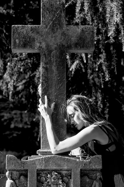 Woman portrait in grief enclosing grave cross monochrome