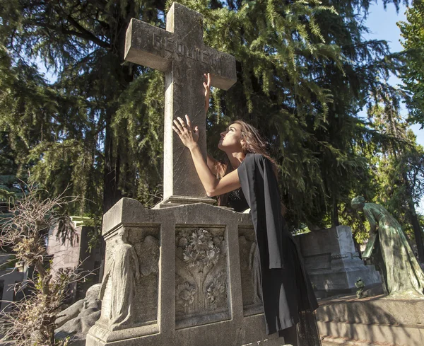 Woman portrait in grief touching and looking at grave cross