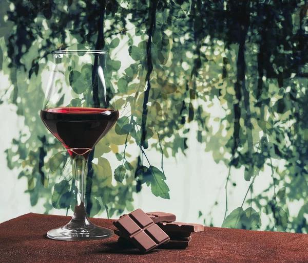 Red wine glass and chocolate with green leaves abstract backgrou