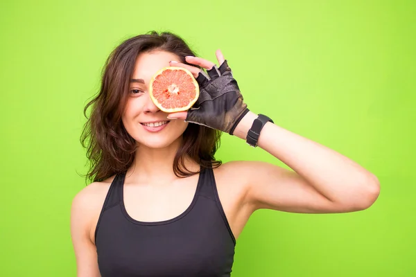Funny portrait of young brunette fitness woman holding fresh pink grapefruit. Healthy eating lifestyle and weight loss concept.Beautiful woman is holding a grapefruit and covering her eye with it
