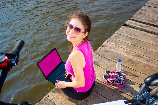 Young woman wearing  in pink shirt sitting on the lake bridge using laptop computer