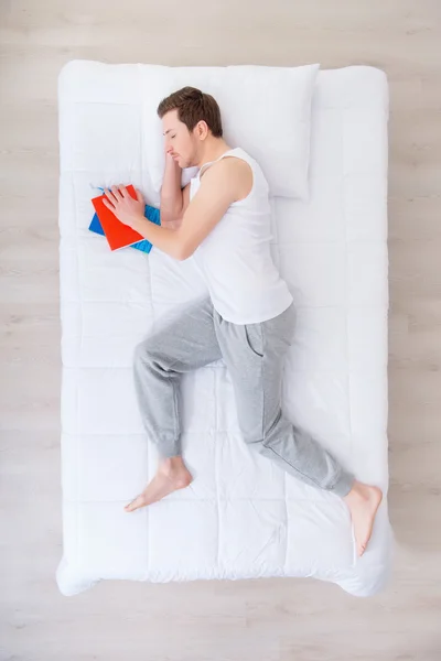 Sleeping man lying in bed with book