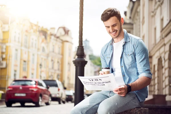 Handsome cheerful man reading newspaper