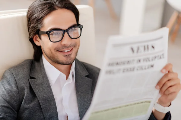 Pleasant smiling man reading newspaper