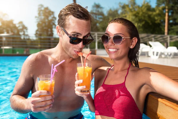 Positive couple drinking cocktails in a swimming pool