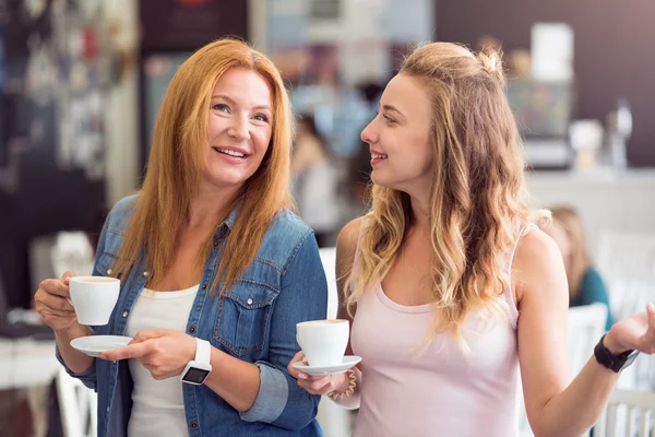 Cheerful mother and daughter drinking coffee