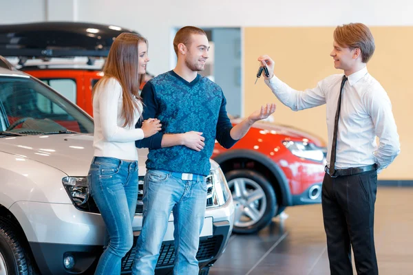 Sales consultant gives keys from new car to young couple