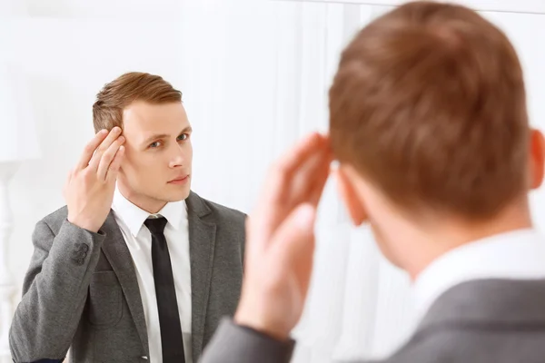 Young man fixing his hair in front of mirror