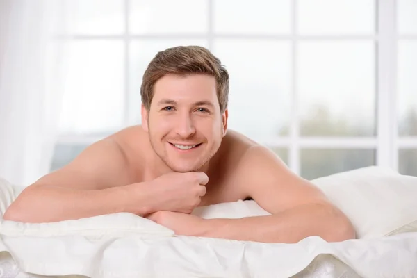 Smiling young man lays awake in bed.