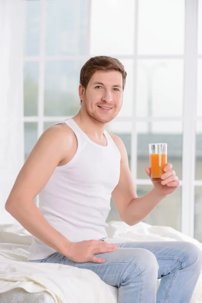 Young man sitting on bed with glass of juice.