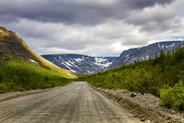 Mountain road. Mountains with snow and overcast skies with storm clouds