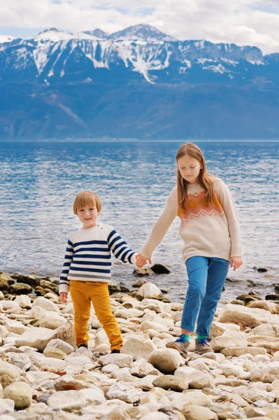 Two adorable kids playing by the lake, little girl and her brother having fun outdoors on a nice spring day